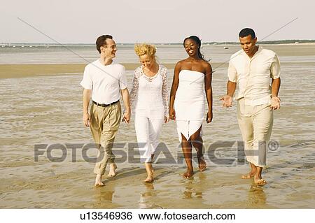 Stock Photograph - Mature couple and their friends walking on the beach. Fotosearch