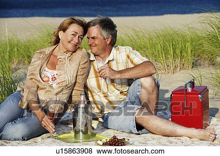 Mature couple sitting on the beach and holding champagne flutes View Large Photo Image Stock Photo - Mature couple sitting on the beach and holding champagne flutes. Fotosearch