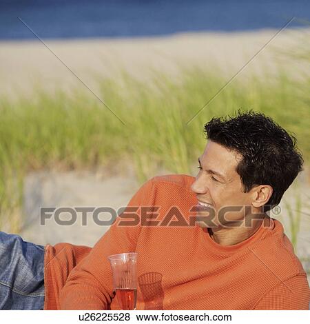 Stock Photo - Mature man lying on the beach and holding a champagne flute. Fotosearch
