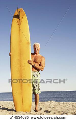 Portrait of a mature man standing on the beach holding a surfboard View Large Photo Image Stock Photography - Portrait of a mature man standing on the beach holding a surfboard. Fotosearch