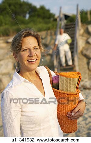Portrait of a mature woman carrying a beach mat and smiling on the beach View Large Photo Image Stock Image - Portrait of a mature woman carrying a beach mat and smiling on the beach. Fotosearch