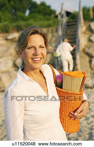 Portrait of a mature woman carrying a beach mat and smiling on the beach View Large Photo Image Stock Photo - Portrait of a mature woman carrying a beach mat and smiling on the beach. Fotosearch