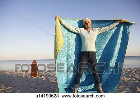 Portrait of a mature woman holding a blanket and smiling on the beach View Large Photo Image Stock Photo - Portrait of a mature woman holding a blanket and smiling on the beach. Fotosearch