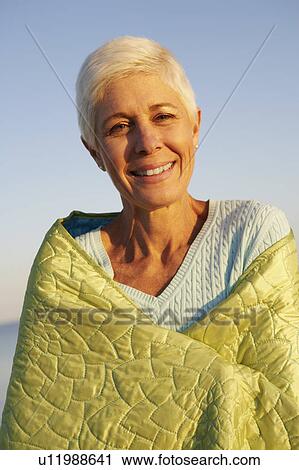 Stock Image - Portrait of a mature woman wrapped in a blanket and smiling. Fotosearch