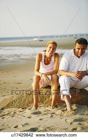 Stock Image - Portrait of a mid adult woman and a mature man sitting on the beach. Fotosearch