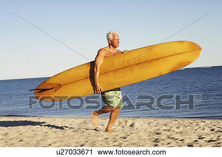 Side profile of a mature man holding a surfboard and walking on the beach View Large Photo Image Stock Image - Side profile of a mature man holding a surfboard and walking on the beach. Fotosearch