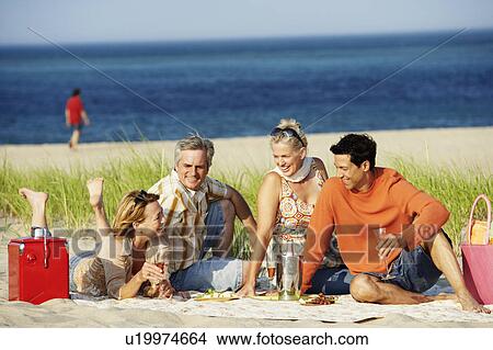 Picture - Two mature couples sitting on the beach. Fotosearch