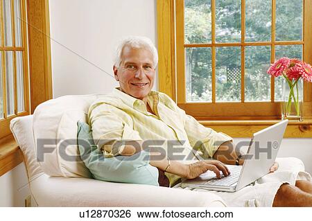 Stock Photograph - Portrait of a mature man using a laptop and smiling. Fotosearch