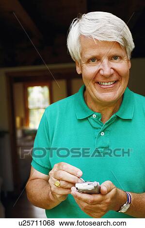 Stock Photo - Portrait of a mature man using a personal data assistant and smiling. Fotosearch