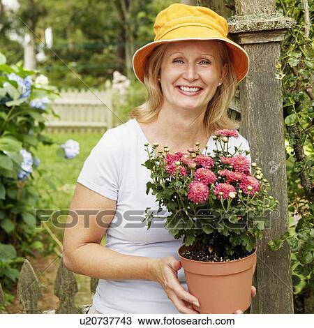 Stock Image - Portrait of a mature woman holding a potted plant and smiling. Fotosearch