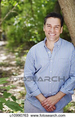 Stock Image - Portrait of a mature woman leaning against a tree and smiling. Fotosearch