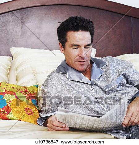 Stock Photo - Close-up of a mature man lying on the bed and reading a newspaper. Fotosearch