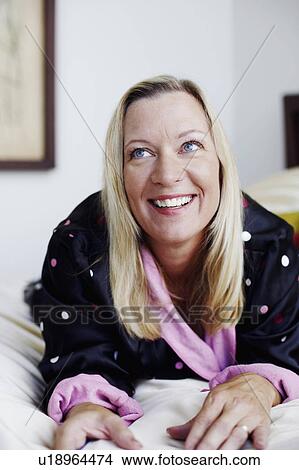 Picture - Close-up of a mature woman lying on the bed and smiling. Fotosearch
