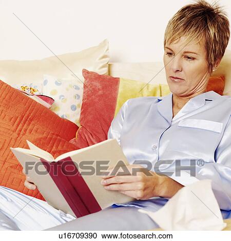 Stock Image - Close-up of a mature woman lying on the bed and reading a book. Fotosearch