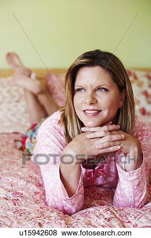 Stock Photo - Close-up of a mature woman lying on the bed and looking away. Fotosearch