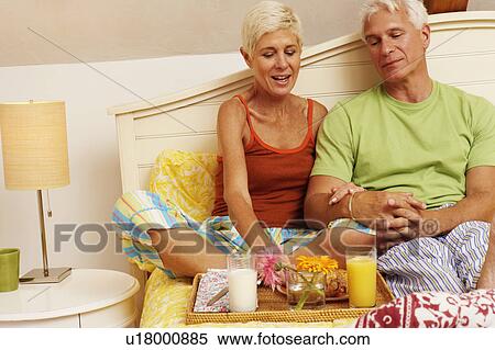 Mature man and a senior woman sitting on the bed and having breakfast View Large Photo Image Stock Photography - Mature man and a senior woman sitting on the bed and having breakfast. Fotosearch