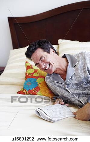 Mature man lying on the bed and holding a newspaper View Large Photo Image Stock Image - Mature man lying on the bed and holding a newspaper. Fotosearch