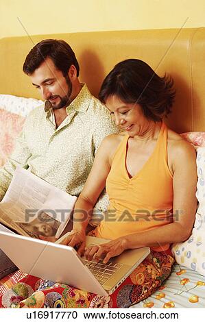 Mature man reading a newspaper with a mature woman using a laptop on the bed View Large Photo Image Stock Image - Mature man reading a newspaper with a mature woman using a laptop on the bed. Fotosearch