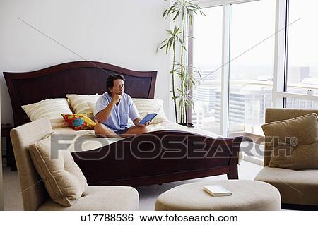 Mature man sitting on the bed reading a book View Large Photo Image Stock Photograph - Mature man sitting on the bed reading a book. Fotosearch