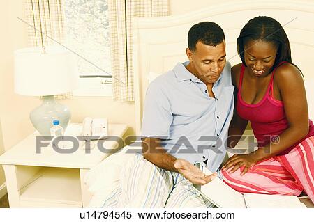 Stock Photography - Mature man with a mid adult woman sitting on the bed and looking at a file. Fotosearch
