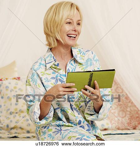 Stock Photograph - Mature woman holding a photo album on the bed. Fotosearch