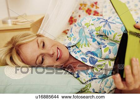 Mature woman lying on the bed and looking a photo album View Large Photo Image Picture - Mature woman lying on the bed and looking a photo album. Fotosearch