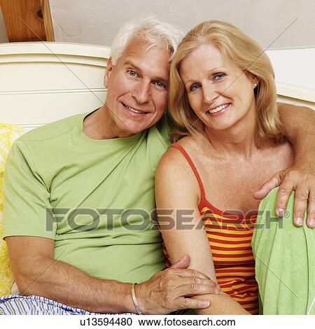 Portrait of a mature couple sitting on the bed and smiling View Large Photo Image Stock Image - Portrait of a mature couple sitting on the bed and smiling. Fotosearch