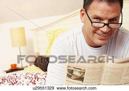 Portrait of a mature man lying in bed and holding a newspaper View Large Photo Image Stock Photo - Portrait of a mature man lying in bed and holding a newspaper. Fotosearch