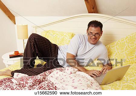 Portrait of a mature man lying on the bed and using a laptop View Large Photo Image Stock Image - Portrait of a mature man lying on the bed and using a laptop. Fotosearch