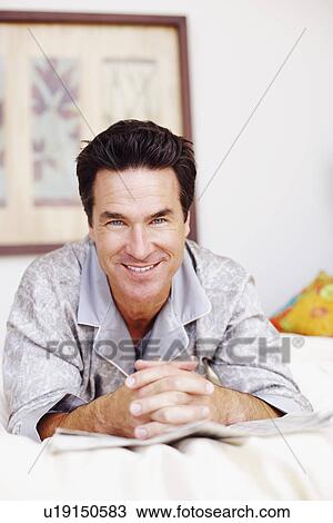 Stock Image - Portrait of a mature man lying on the bed and smiling. Fotosearch
