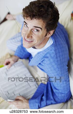 Stock Image - Portrait of a mature man lying on the bed holding a newspaper. Fotosearch