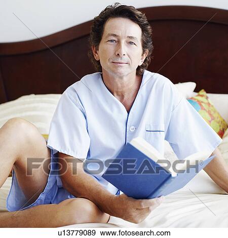 Stock Photo - Portrait of a mature man sitting on the bed holding a book. Fotosearch