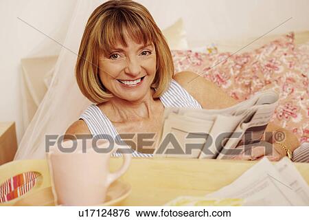 Stock Photograph - Portrait of a mature woman holding a newspaper and smiling. Fotosearch