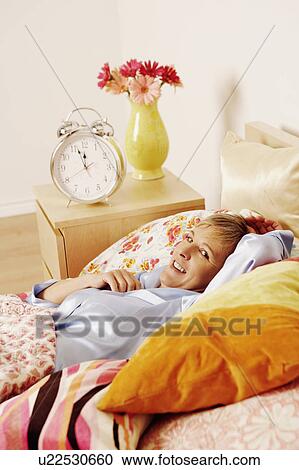 Stock Image - Portrait of a mature woman lying in bed and smiling. Fotosearch