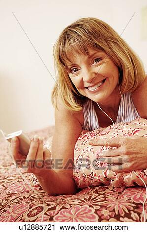 Portrait of a mature woman lying on the bed listening to an MP3 player View Large Photo Image Stock Image - Portrait of a mature woman lying on the bed listening to an MP3 player. Fotosearch