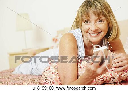 Portrait of a mature woman lying on the bed listening to an MP3 player and smiling View Large Photo Image Stock Image - Portrait of a mature woman lying on the bed listening to an MP3 player and smiling. Fotosearch