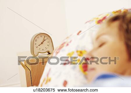 Stock Photography - An alarm clock beside a mature woman sleeping on the bed. Fotosearch