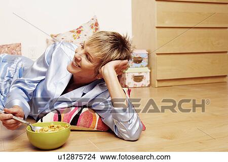 Close-up of a mature woman lying on the floor and eating corn flakes View Large Photo Image Picture - Close-up of a mature woman lying on the floor and eating corn flakes. Fotosearch