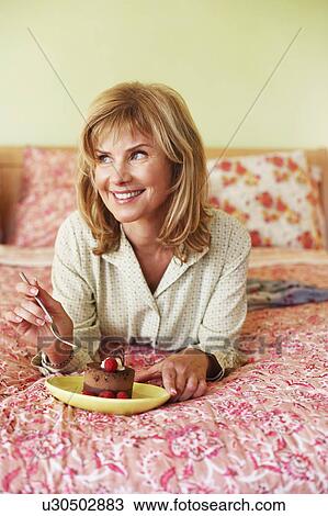 Close-up of a mature woman lying on the bed and eating cake View Large Photo Image Stock Image - Close-up of a mature woman lying on the bed and eating cake. Fotosearch