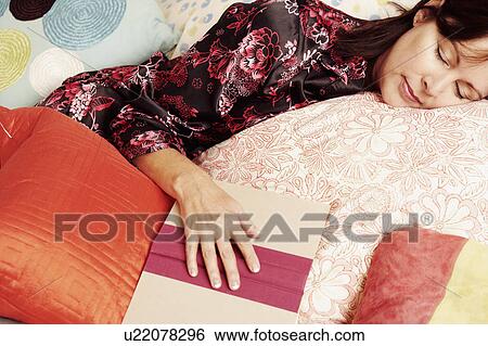 Stock Photograph - Close-up of a mature woman sleeping on the bed with a book. Fotosearch