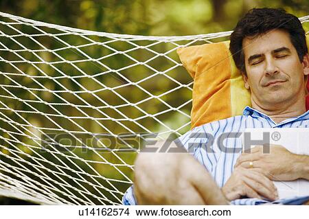 Mature man holding a magazine and sleeping in a hammock View Large Photo Image Picture - Mature man holding a magazine and sleeping in a hammock. Fotosearch