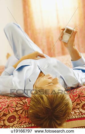Stock Photo - Mature woman lying on the bed listening to an MP3 player. Fotosearch