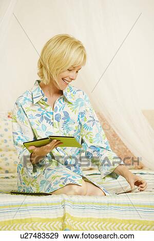 Stock Photo - Mature woman sitting on the bed and holding a photo album. Fotosearch