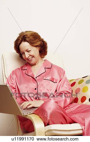 Stock Image - Mature woman using a laptop and smiling. Fotosearch