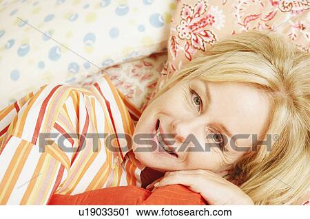 Stock Image - Portrait of a mature woman lying in bed and smiling. Fotosearch