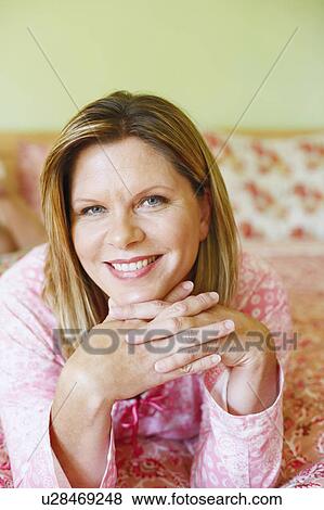Stock Photo - Portrait of a mature woman lying on the bed and smiling. Fotosearch