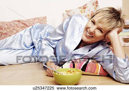 Stock Photography - Portrait of a mature woman lying on the floor with a bowl of corn flakes. Fotosearch