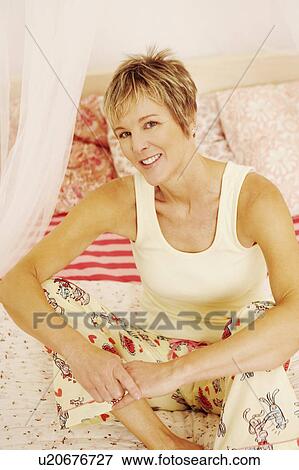 Stock Photo - Portrait of a mature woman sitting on the bed and smiling. Fotosearch