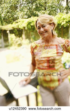 Stock Image - Portrait of a mature woman using a laptop with her hand on her hip. Fotosearch