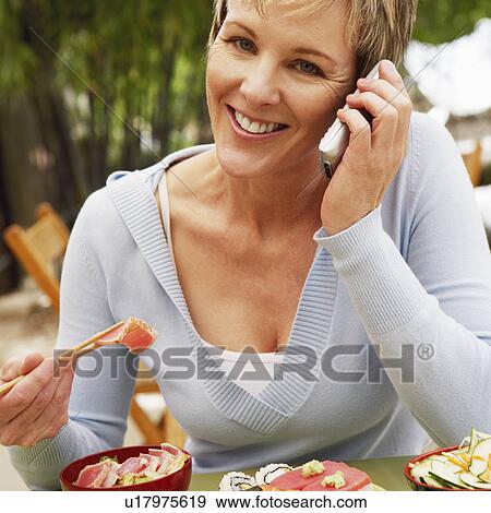 Close-up of a mature woman eating with chopsticks and talking on a mobile phone View Large Photo Image Stock Photo - Close-up of a mature woman eating with chopsticks and talking on a mobile phone. Fotosearch